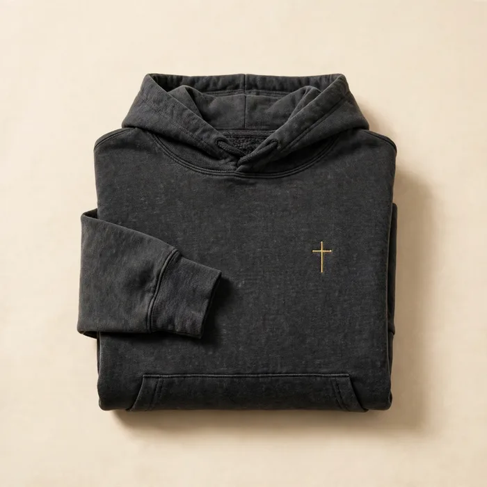 Folded charcoal hoodie with a small gold cross on the chest